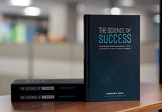 A hardcover copy of The Science of Success by Charles Koch, standing upright against a neutral gradient background.