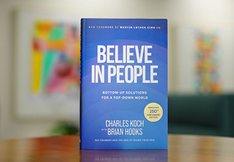 A hardcover copy of Believe in People, co-authored by Charles Koch and Brian Hooks, standing upright against a neutral gradient background.