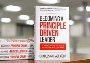A hardcover copy of Becoming a Principle-Driven Leader, co-authored by Charles Koch and Chase Koch, standing upright against a neutral gradient background.
